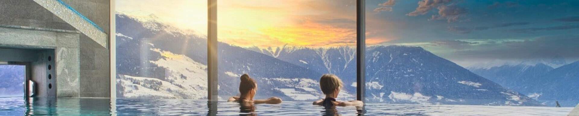 Zwei Frauen von hinten in einem Pool, die den Blick auf die schneebedeckten Berge in einem Luxus-Wellnesszentrum genießen